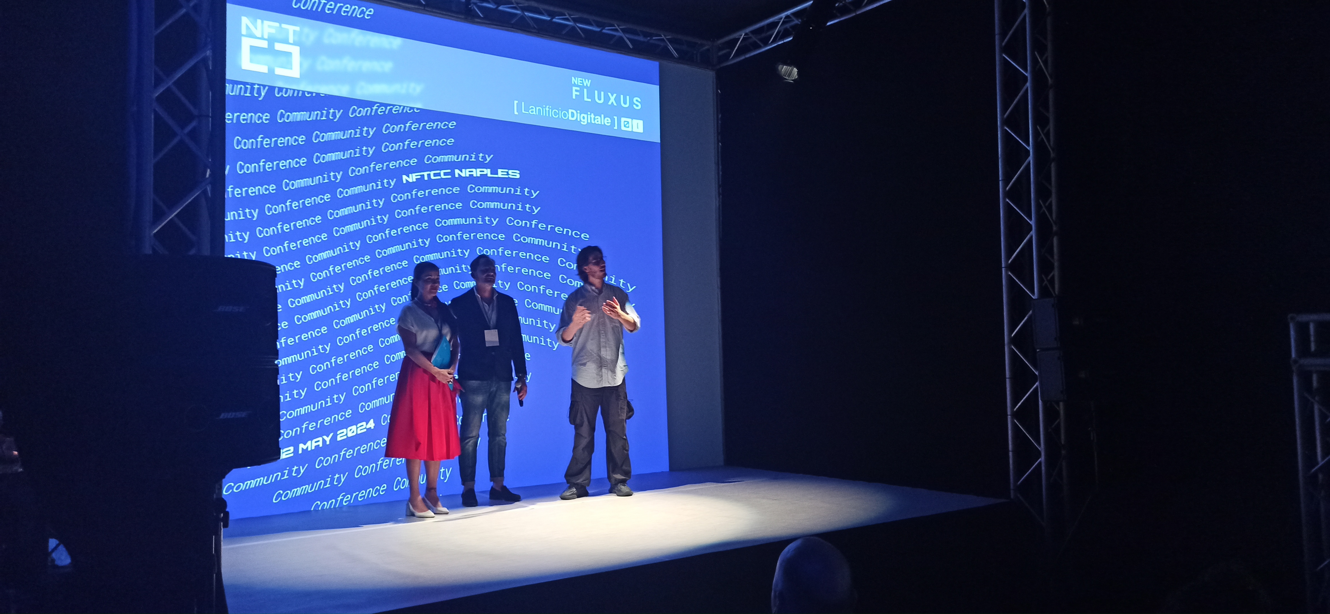 People on the Lanificio Digitale stage in front of a digital art projection during New Fluxus